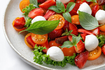 Fresh summer salad with strawberry, tomatoes cherry, mozzarella cheese and basil. Fresh bright healthy salad. Close up.