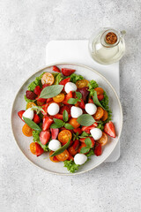 Healthy summer salad with strawberry, tomatoes cherry, mozzarella cheese and basil. Fresh bright salad. Top view.