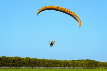 View of man paragliding over Midwestern soybean field with working sprinkler irrigation system;...