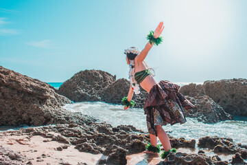 Hula dancer on the beach. Woman in bikini dancing Hawaiian typical of Tahiti. Tropical lady at beach with flower crown on her head and neck. Ready to party. Exotic girl in swimwear.