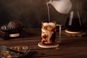 Iced coffee. Next to him is a coffee pot, marshmallows and caramelized sugar. Pouring cream into...