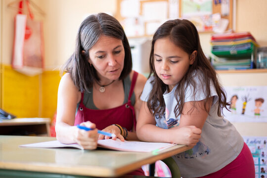 Young adult female teacher helping a primary school pupil in class to learn a lesson. Concept of education and development in children.