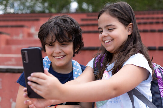 Close-up of smiling caucasian boy and girl primary school students taking a photo together with a mobile phone outdoors. Concept of the use of technology in children.