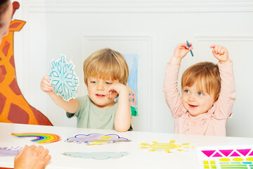 Two kids show weather cards sitting in the kindergarten class
