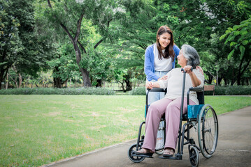 Fototapeta premium Asian family, attractive daughter looking and taking care her mother is patient with paralysis, Sitting on a wheelchair, at green garden, to relationship in family and health care concept