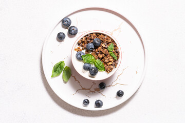 Homemade granola with yogurt and blueberries on the marble tray on white stone background top view. Healthy tasty breakfast concept.