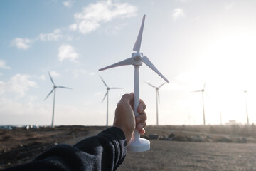 Hand holding wind turbine prototype model miniature with wind power station at background