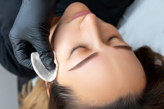 cleansing the model's skin with a cotton sponge after eyebrow tattooing using a permanent makeup machine