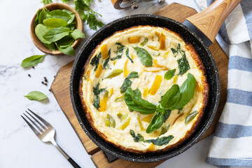 Spinach and cheese omelette. Frittata made of eggs, paprika and spinach in a frying pan on a marble...