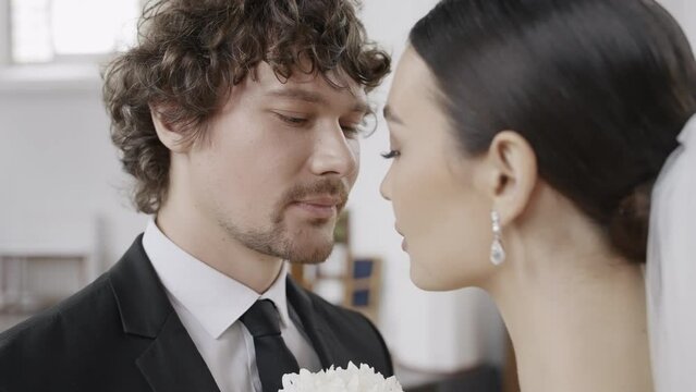 Side view of a loving couple kissing each other during marriage process in a church. Action. Groom and bride first kiss.