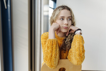 Young teenage girl sits on an office chair and looks thoughtfully to the side