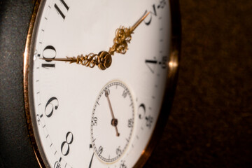 The white dial face of an antique round pocket watch with hands and numbers. Close up of a black and gold retro watch with golden hands. Luxury aged timepiece. Mechanical old metal clock.