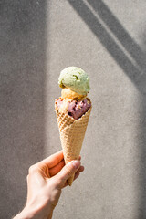 Man's hand holding melting vanilla ice cream with multi-colored balls in a waffle cone on a gray...