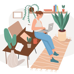 Happy woman is working online, leaning against a table with a laptop. The workplace of a female freelancer working from a home office, remotely .The concept of a home office, a woman working from home
