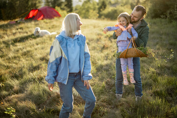 Young caucasian couple with little girl have fun while travel in the mountains. Happy family spending summer vacation at campsite. Father tossing daughter in his arms