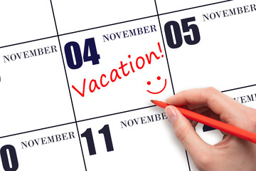 A hand writing a VACATION text and drawing a smiling face on a calendar date 4 November. Vacation planning concept.