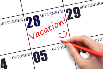 A hand writing a VACATION text and drawing a smiling face on a calendar date 28 September ....