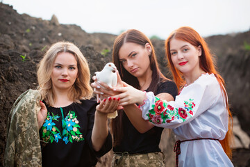 Three beautiful Ukrainian women in a trench with a white dove in their hands