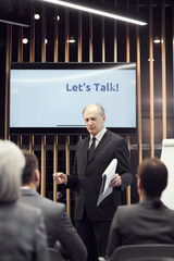 Content balding senior executive in formal suit holding clipboard and explaining key aspects in...