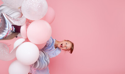 Joyful child girl in elegant tulle dress near the balloons. Birthday present. Funny face celebrates birthday party on pink background.