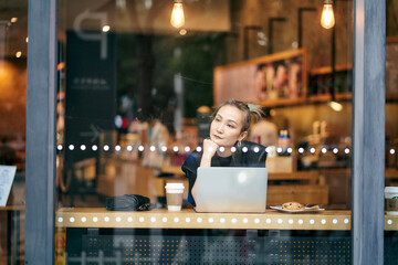 asian business woman sitting by the window in coffee shop working using laptop computer