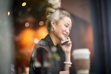 asian woman talking chatting on cellphone in coffee shop happy and smiling