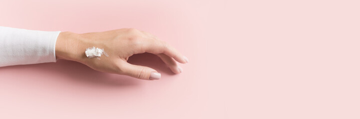 Hand of beautiful young girl with cream on pink pastel background. Concept template feminine blog, social media, beauty concept. Web banner