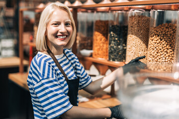 Beautiful blonde woman working at health food store. Plastic free shop. Healthy food concept. 