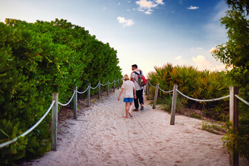 lushy tropical pathway to sandy beach at summer morning with people walking to the beach on the background