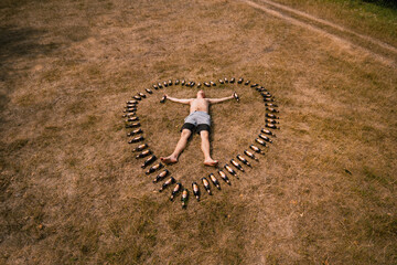 A drunk man is lying on the ground. Heart made of beer bottles. Love of alcoholic beverages, fun and alcoholism. Nature, rest.
