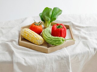 Wooden board with tomato, pepper, bitter gourd, corn and lettuce on white background