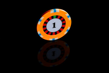 One yellow casino chip with unit on isolated black table background with reflective surface. Extra close up of chip for playing roulette, poker, blackjack. Gambling background.