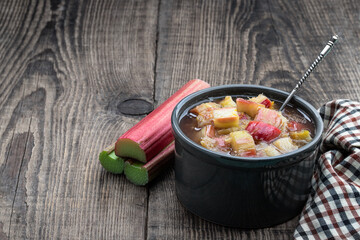 Homemade rhubarb jam in ceramic bowl with raw stalk rhubarb on wooden table