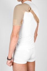 Shoulder joint orthosis or brace isolated on white background. A man in a support orthopedic bandage on his arms after surgery, suffering from shoulder pain, the result of a work injury - obrazy, fototapety, plakaty