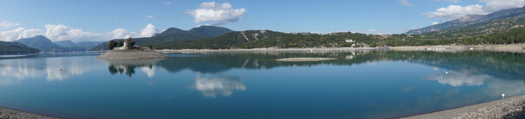Fototapeta na wymiar panoramic view of the mirror reflection of the mountains and island of bay st michel in serre ponçon lake alps france