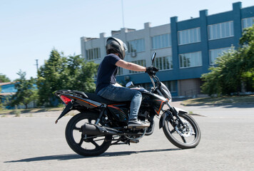 Fototapeta na wymiar A guy in a helmet trains to ride a motorcycle, turns around on an empty asphalt road