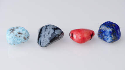 four gemstones in a row on white background, they are larimar, snowflake obsidian, coral and lapis lazuli