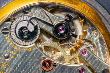 Rear viev of a old pocket watch with an open clockwork. Retro clock with engraving inside, view of gearing, round wheel gears. Mechanism of mechanical golden vintage watch close up.