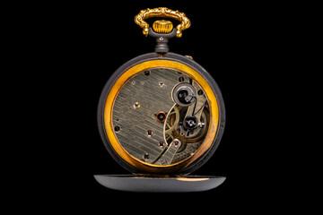 Rear view of an open antique mechanical pocket watch on isolated black background. Black golden retro timepiece with mechanism and gears. Old round clock inside view. Vintage expensive watch.