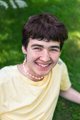 portrait of cheerful young man with earrings in his ears, multicolored necklace around his neck on outdoors, LGBT theme, bisexual man
