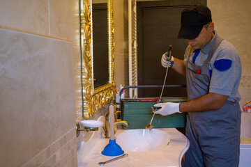 Image of a smiling plumber who unclogged a clogged sink with a probe. Do-it-yourself work