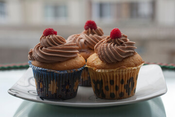 Beige cupcakes made of delicate light sponge cake decorated with chocolate cream. Topped with ripe raspberries.