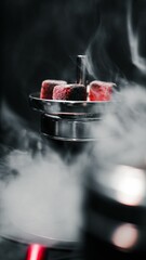 Vertical shot of bright red charcoal cubes on metal shisha in dark smoky gaming room