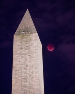 Vertical shot of the Washington Monument Obelisk under dark blue sky with red moon
