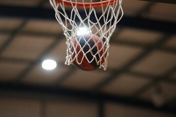 A basketball lands in a basketball net during a basketball game in an indoor stadium