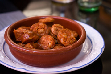 Delicious chorizos in cider in a traditional clay bowl on a white plate. Typical Spanish tapas from...
