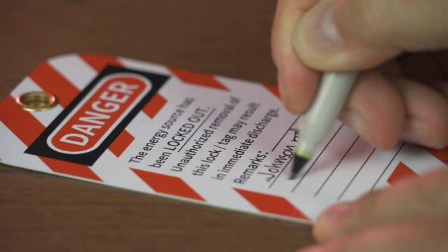 A contractor or repairman writes notes on a lockout tagout tag warning others not to use an out-of-service machine.  	