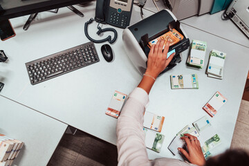 Bank employees using money counting machine while sorting and counting paper banknotes inside bank...