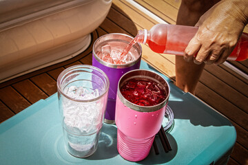 Boat Drinks poured from a bottle into insulated glasses with ice sitting on an ice chest on a...