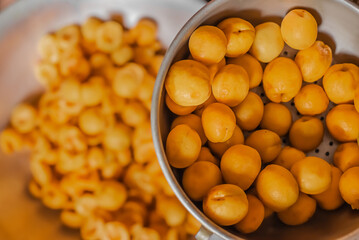 Freshly picked apricots lie in sieve dripping in big metal basin after washing under water.Pile of juicy,ripe fruits halves,slices the workpiece to jam.Summer harvest,canning concept.Farmer worked